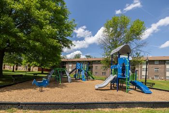 A playground with a blue slide and a green tree.at Deer Park Apartments, Randallstown